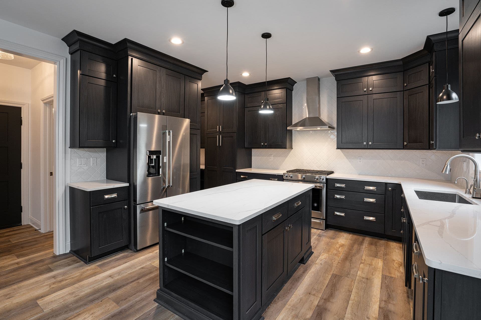 A modern kitchen with dark wood cabinets, a stainless steel refrigerator, and an island with a white countertop. Pendant lights create a warm ambiance.
